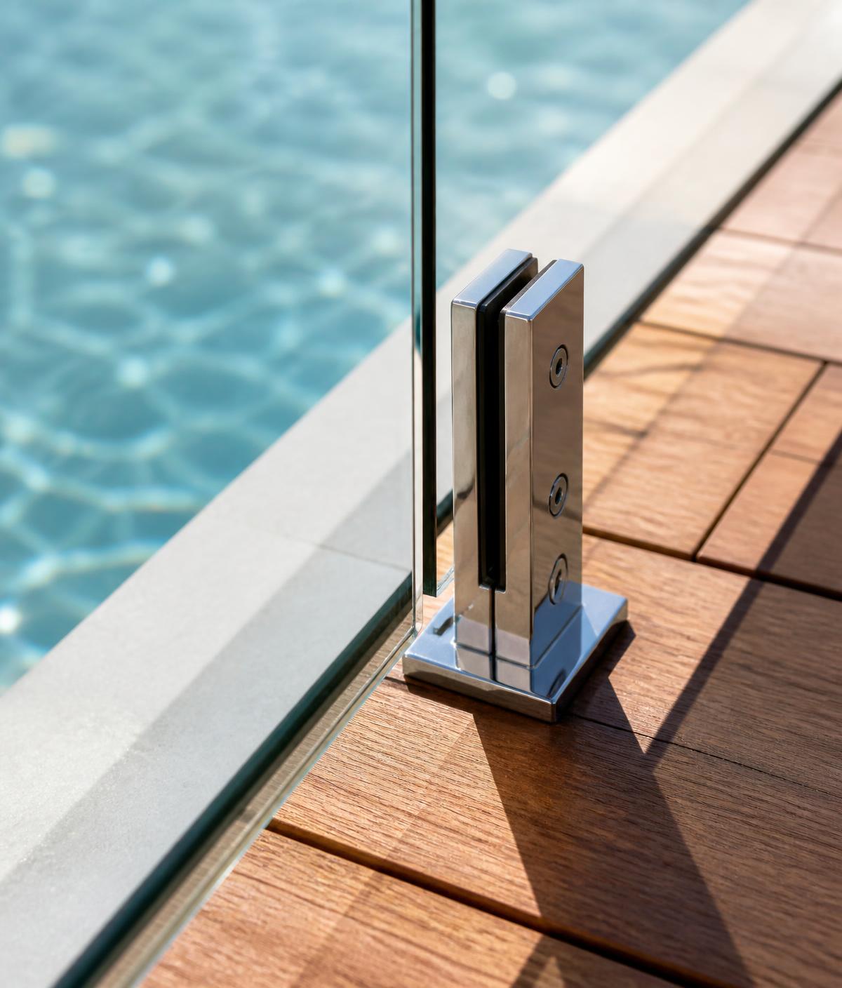 Polished stainless steel spigot holding a frameless glass pool fence panel on timber decking